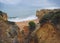 Beautiful sandstone cliffs with view on two people standing on sand beach with sea waves and rock formation and blue sky