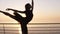 Beautiful scene of a dancing ballerina in tutu and pointe near ocean or sea at sunrise or sunset. Young sensual woman