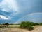 Beautiful scene of double rainbow on blue sky copy space background above natural sand road, grass and tree on savanna plain