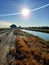 Beautiful scene of water canal and dirt road facing the sunshine