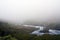 Beautiful scenery of a green landscape with a river enveloped in fog in Norway