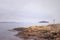 Beautiful, scenic landscape by Oslo Fiord. Orange rock formations on the beach, distant island, calm water, silhouette of a cormor