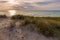 Beautiful sea view with a pirate ship sailing at sunset, dunes covered with tall grass in the foreground,