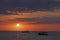 Beautiful seascape with boat in the sea at sunset with a colorful evening sky and a round disk of sun over the sea.