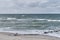 Beautiful seascape with old wooden breakwater, waves, sandy beach and cloudy sky.