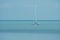 Beautiful seascape view of lonely white sailboat floating on blue sea in sunny day.