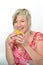 Beautiful senior woman smiling in pink suit eating yellow macaroon