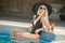 Beautiful sensual blonde with sunglasses and black hut relaxing in the pool with a juice. Attractive long hair woman in black