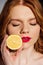 Beautiful sensual redhead girl with red lips and eyes closed posing with cut lemon.