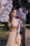 Beautiful sensual woman with dark hair in elegant dress posing in garden with flowering wisteria trees