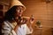 Beautiful serene Hispanic woman enjoys the aroma of essential oil in a wooden mortar while steaming in a wooden sauna. Close-up