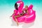 Beautiful sexy, amazing young woman in a swimming pool sitting on an inflatable pink flaming and laughing, tanned body, long hair