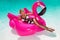 Beautiful sexy, amazing young woman in a swimming pool sitting on an inflatable pink flaming and laughing, tanned body, long hair