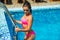 Beautiful sexy girl with long hair in luxurious swimming suit relaxing in swimming pool. Woman with tanned fit sexy body. Summer