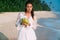 Beautiful shining young brunette girl with natural make-up walks along the seashore, drinks a delicious fresh coconut