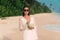Beautiful shining young tanned girl on the beach wearing a white shirt and fashion sunglasses, holding a fresh coconut