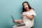 Beautiful shocked teenager girl with long black hair in white dress sitting with laptop, pointing at display and looking at camera