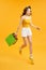 Beautiful shopaholic young woman jumping in the air with shopping bags over orange background