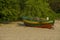 Beautiful shot of a colorful dinghy boat at the sandy shore under the inclining trees