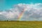 Beautiful shot of an empty grassy field with a rainbow in the distance under a blue cloudy sky