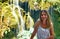 Beautiful shot of a female in a white shirt standing close to a waterfall, smiling