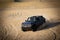 Beautiful shot of a grey Bronco truck with a USA flag in dunes kicking up sand