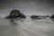 Beautiful shot of rock formations on the body of water with flowing movement under a gray cloudy sky