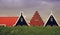 Beautiful shot of three gable roofs behind a grassy hill under the cloudy sky