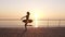 Beautiful silhouette of ballerina in ballet tutu and point on embankment above ocean or sea at sunrise. Young beautiful