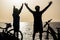 Beautiful silhouette of couple of seniors at the beach with their bikes and with their arms up - winners and successful concept
