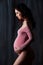 Beautiful silhouette of a pregnant woman on a dark background. A brunette girl in a pink body suit gently embraces a pregnant