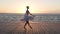 Beautiful silhouette of young ballerina in white tutu. Doing classic ballet moves. Embankment near the sea or ocean. Sun