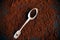 A beautiful silver teaspoon with a portion of ground coffee in it lies against a background of scattered coffee. Instant coffee in