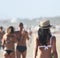 Beautiful single girl, seen from behind, with hat who walk on the beach. A love couple in the background.