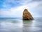 A beautiful single rock formation and splashing swash silky smooth water reflection on beach.