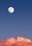 Beautiful sky landscape with white full moon high on clear blue gradient sky above red clouds on sunset