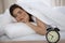 Beautiful sleeping woman lying in bed and trying to wake up with alarm clock. Girl having trouble with getting up early