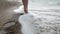 Beautiful slender female legs walk along the small waves of the sandy shore. Sexy female feet go along the strip of the