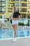 A beautiful slender fitness athletic blonde girl in white shorts and a black short T-shirt, standing by the pool at the hotel in