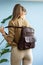 beautiful slender girl in beige pants and olive sweater posing with a small shiny brown leather backpack
