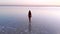 A beautiful slender model walks on a salt lake against the sunset. Young blonde girl during natural Spa treatments. Eco-tourism.