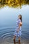 Beautiful slender woman in a long blue dress walks near the lake. Brown-haired girl with long hair walks in the water. natural