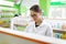 A beautiful slim brown-haired girl with glasses, wearing a lab coat, looks intently at the shelf in a modern pharmacy.
