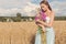 Beautiful slim girl in a blue dress in the field with a bouquet of flowers and ears of corn in his hands at sunset on a sunny