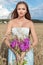 Beautiful slim girl in a blue dress in the field with a bouquet of flowers and ears of corn in his hands at sunset on a sunny