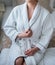 Beautiful slim girl in white robe after shower sitting on bed.