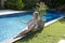 Beautiful slim woman in an open bathing suit sits on the edge of the pool and looks at the spray of water