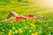 Beautiful slim young female student in a bright red dress cuts in the middle of a green field or meadow in yellow dandelions