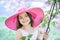 Beautiful small teen girl in pink fashionable hat with smiling face in spring flower blossom on sunny day. Spring