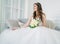 Beautiful smiling brunette woman bride in wedding dress with classical white roses bouquet in living room